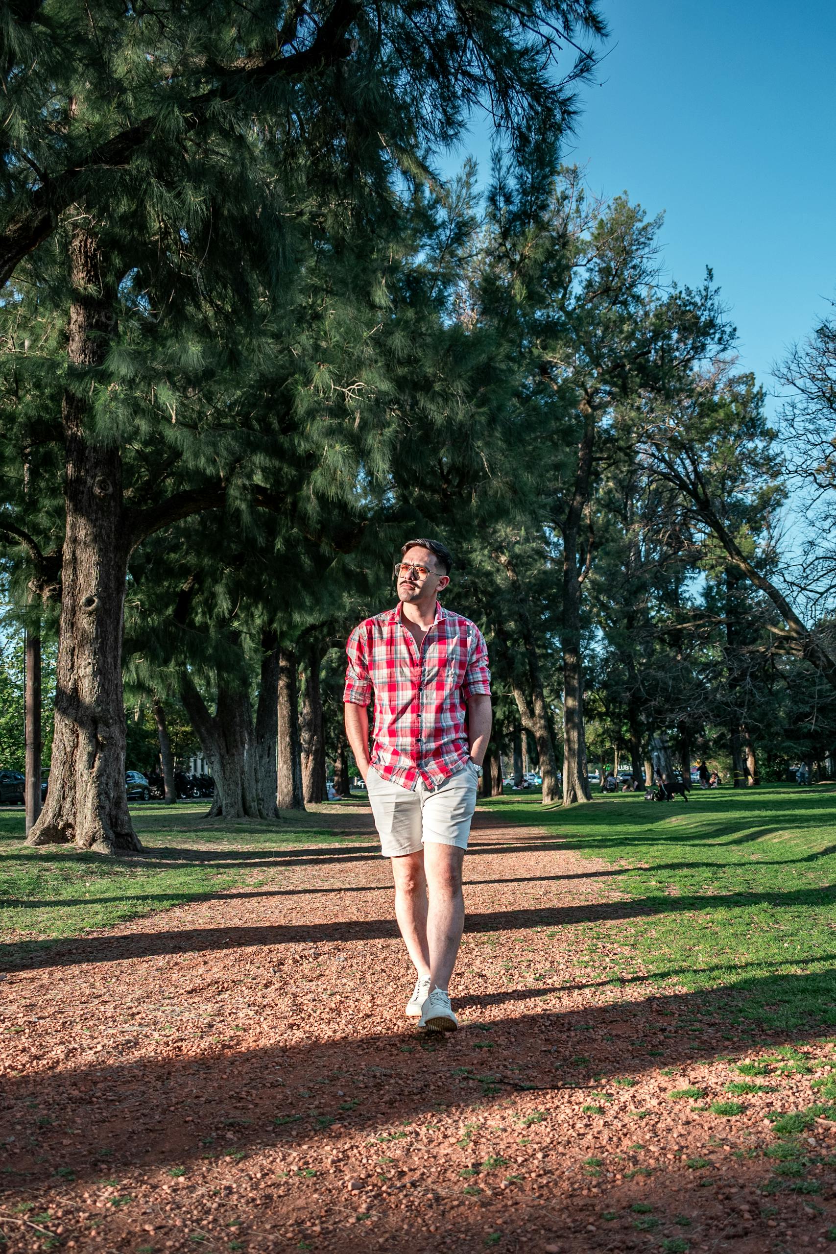 Man enjoying a walk on a sunny day in a tree-filled park.