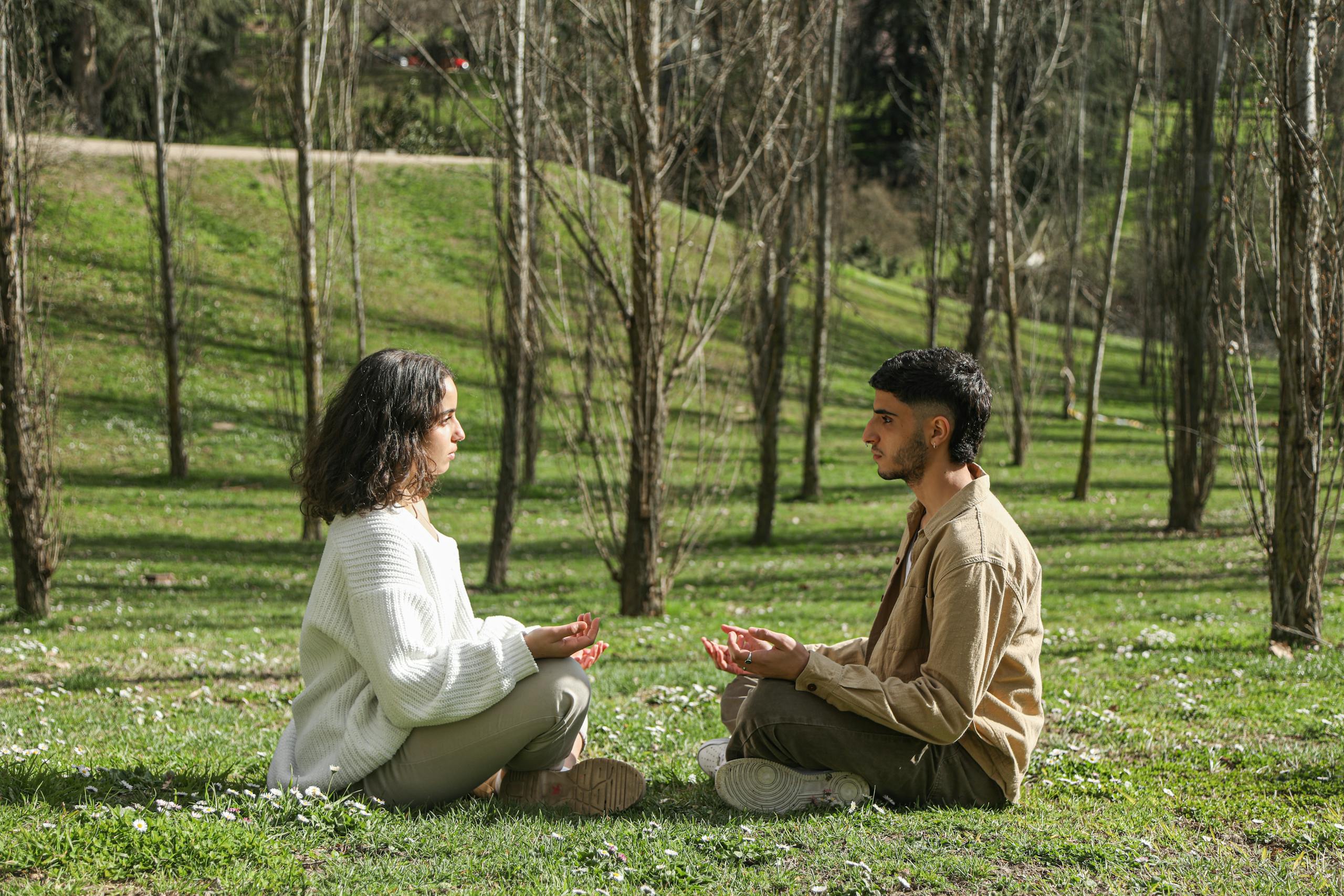 Two people meditate facing each other in a peaceful park setting, embracing tranquility.