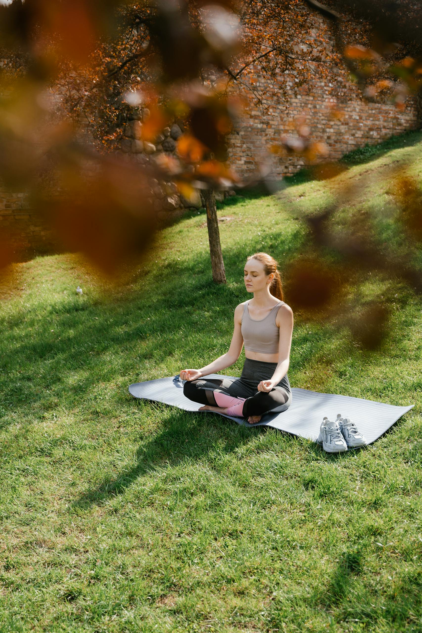 Woman practicing yoga outdoors in a serene park setting, meditating on a mat.
